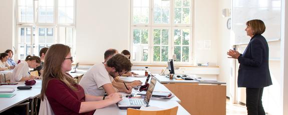Prof. Dana Beldiman standing at the front of a classroom leading a course on IP law; before her, around ten students listen from their desks and take notes as she gesticulates