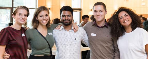 Five students stand arm in arm in front of the buffet at the International Dinner extracurricular event
